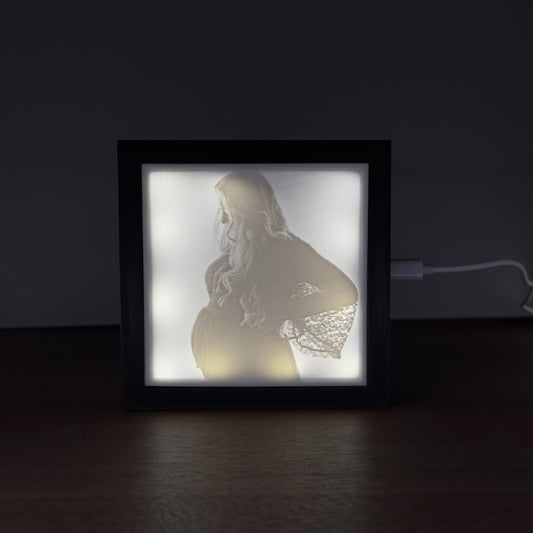Verlicht fotoframe met 3D-geprinte lithofane van een zwangere vrouw – sfeervol uitgelicht portret op donker oppervlak.