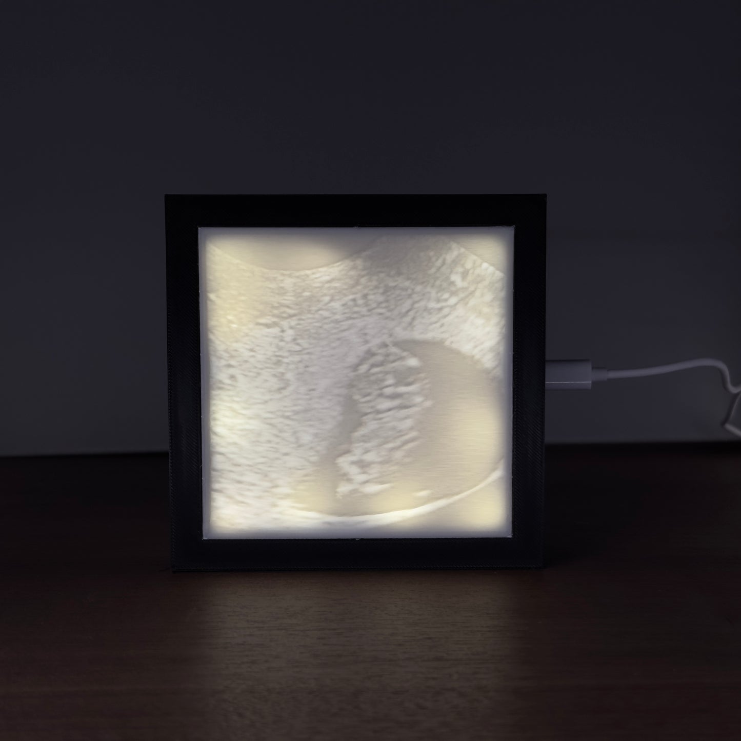 Verlicht fotoframe met 3D-geprinte lithofane van een echo-afbeelding – sfeervol verlicht in een donkere ruimte.