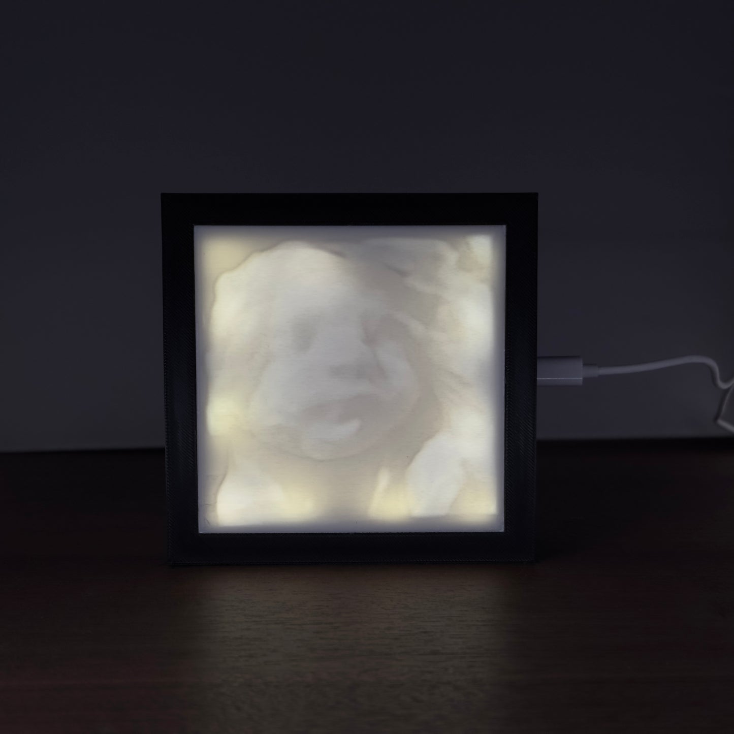 Verlicht fotoframe met een 3D-geprinte lithofane van een 3D-echo – toont het gezicht van een ongeboren baby in sfeervol licht.