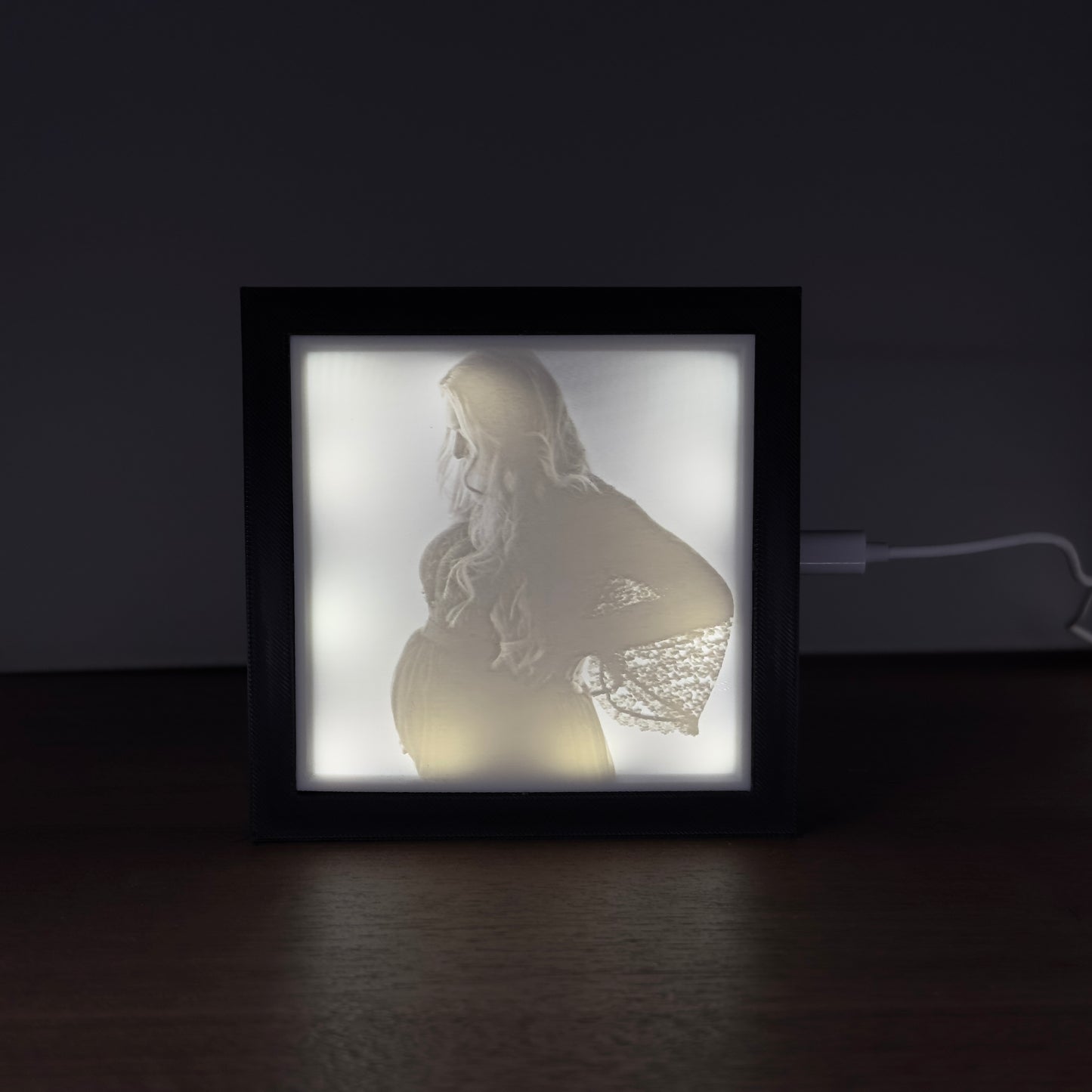 Verlicht fotoframe met 3D-geprinte lithofane van een zwangere vrouw – sfeervol uitgelicht portret op donker oppervlak.
