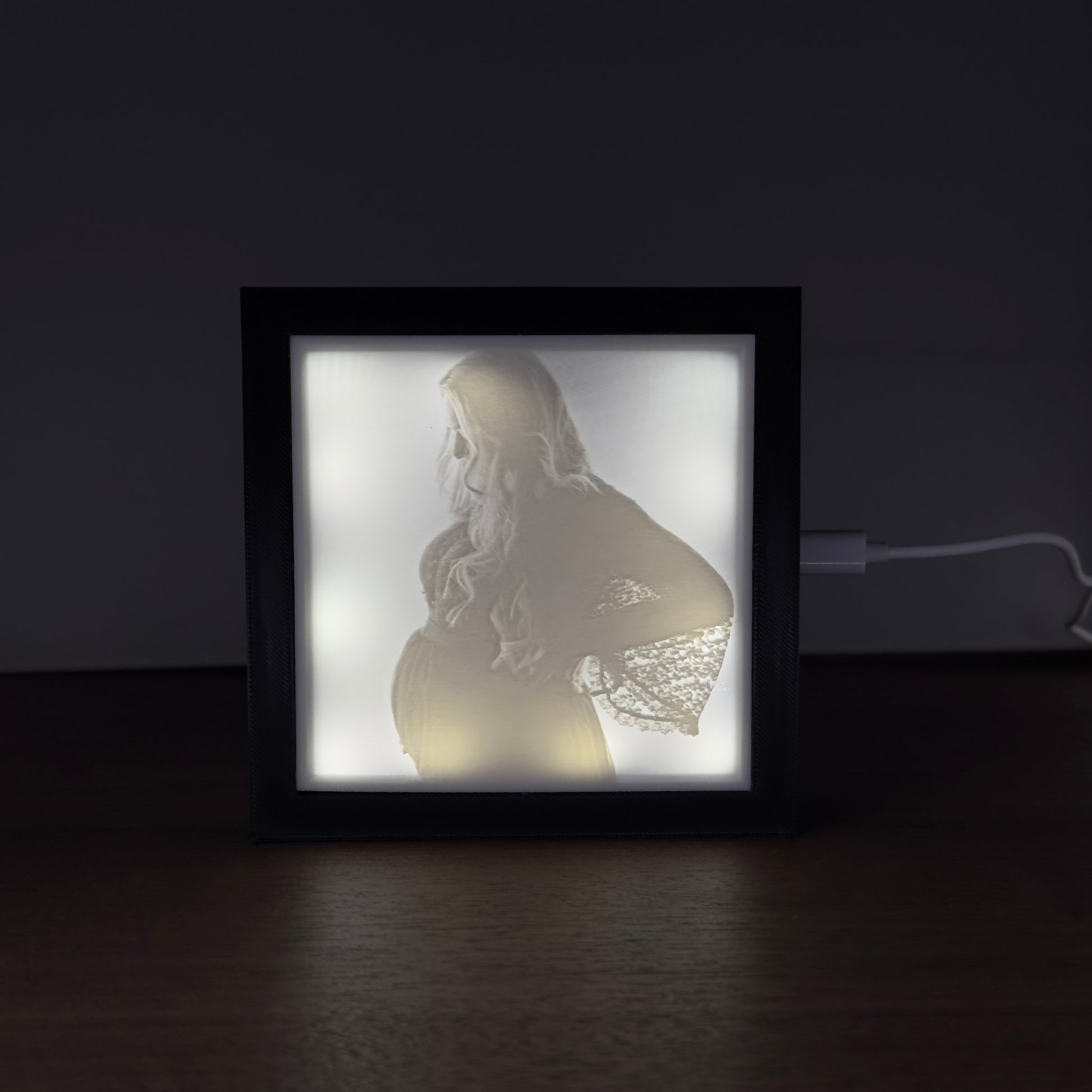 Verlicht fotoframe met 3D-geprinte lithofane van een zwangere vrouw – sfeervol uitgelicht portret op donker oppervlak.