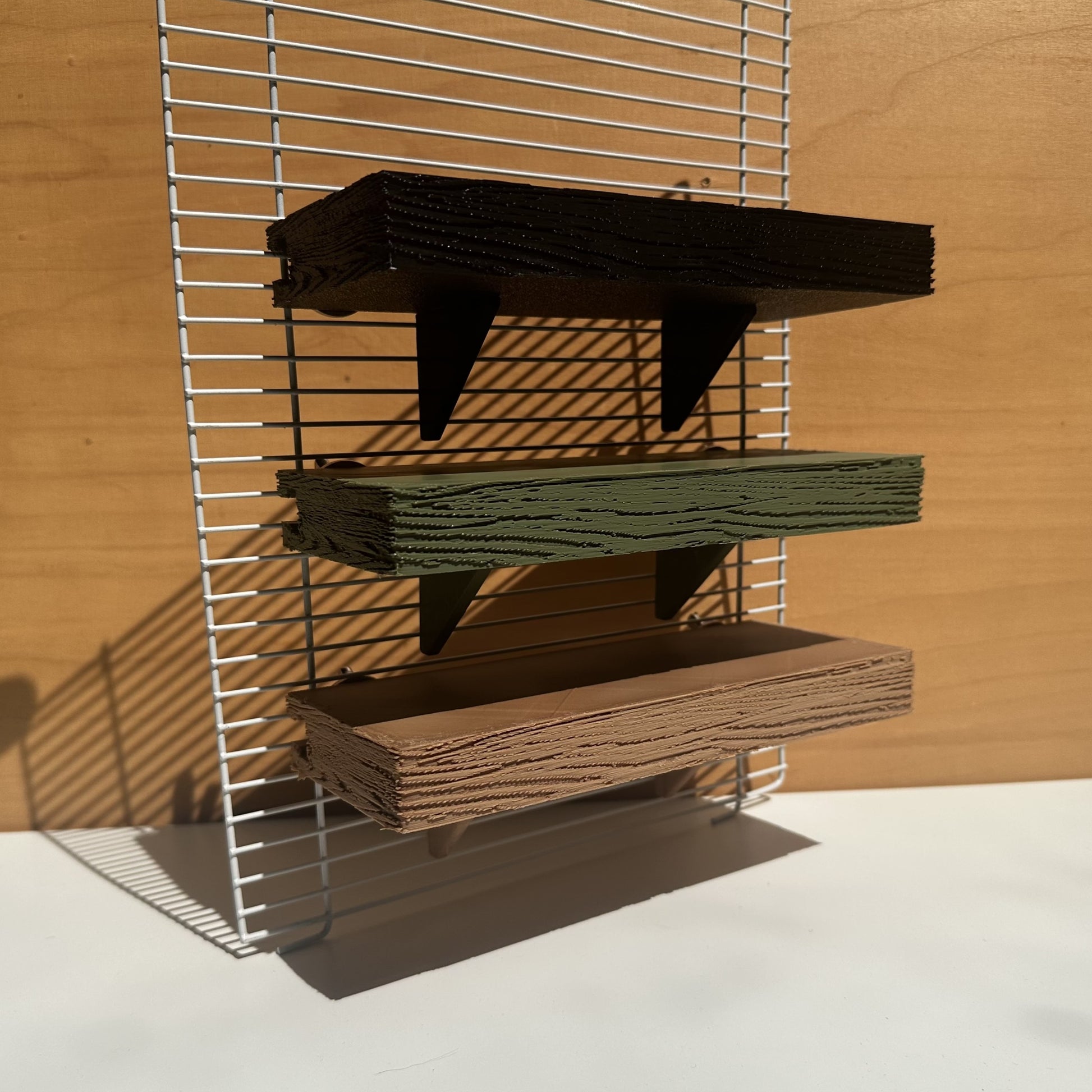 Verstelbare knaagdierplankjes in houtkleur, olijfgroen en zwart – als demonstratie bevestigd aan tralies op verschillende hoogtes.